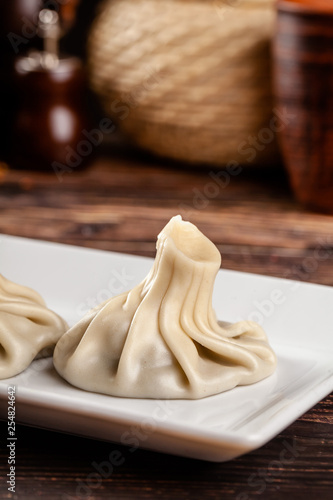 The concept of Georgian cuisine. Khinkali from white dough with meat. Serving dishes in Georgian restaurant on a white plate, on a wooden table. Background image. copy space