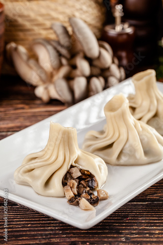 The concept of Georgian cuisine. Khinkali from white dough with mushrooms. Serving dishes in Georgian restaurant on a white plate, on a wooden table. Background image. copy space