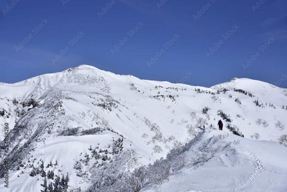 上州武尊山の山頂に向かって雪の尾根を歩く登山者。