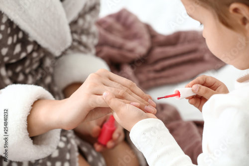 Cute daughter with mother making manicure at home