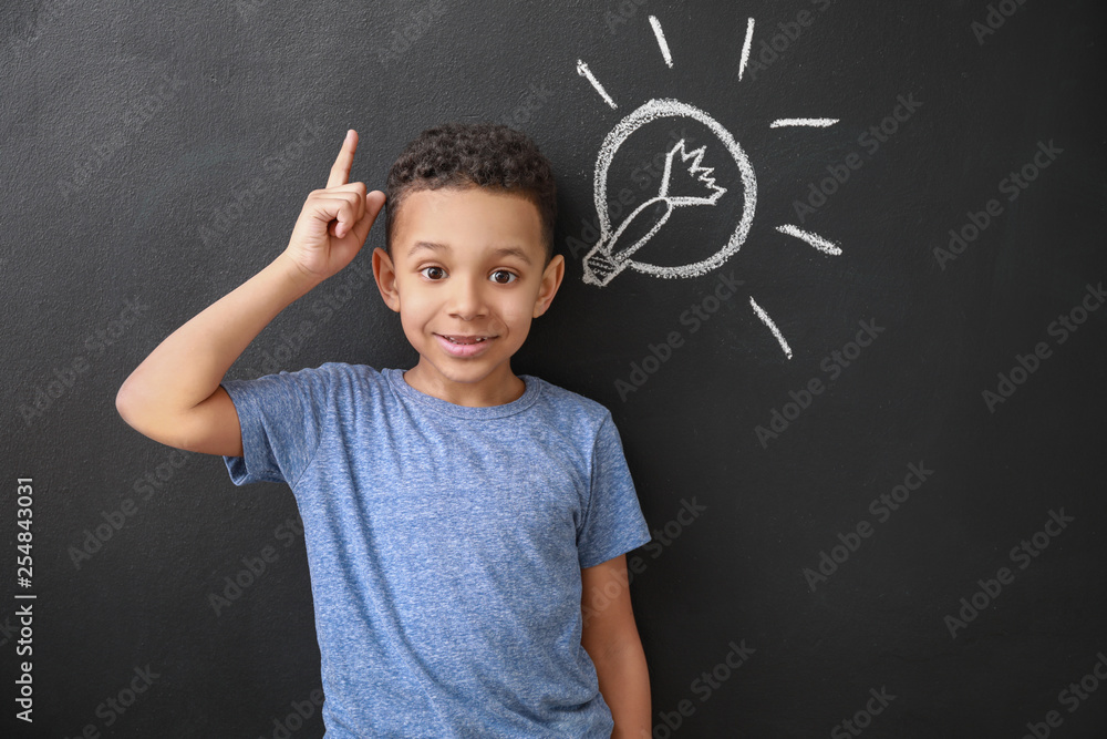Happy African-American boy with raised index finger near drawn light bulb on dark wall