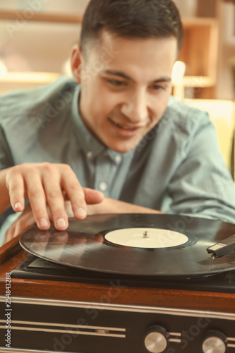 Young man listening to music on record player at home