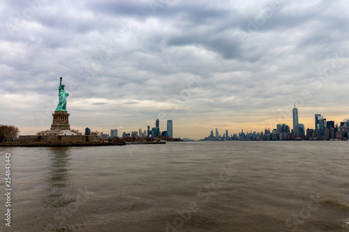 View of New York City skyline and Statue of Liberty with dramatic sky at dusk, New York, USA © Andrew Davidson