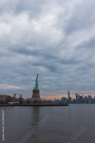 View of New York City skyline and Statue of Liberty with dramatic sky at dusk, New York, USA