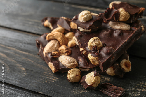 Pieces of tasty dark chocolate with nuts on wooden background