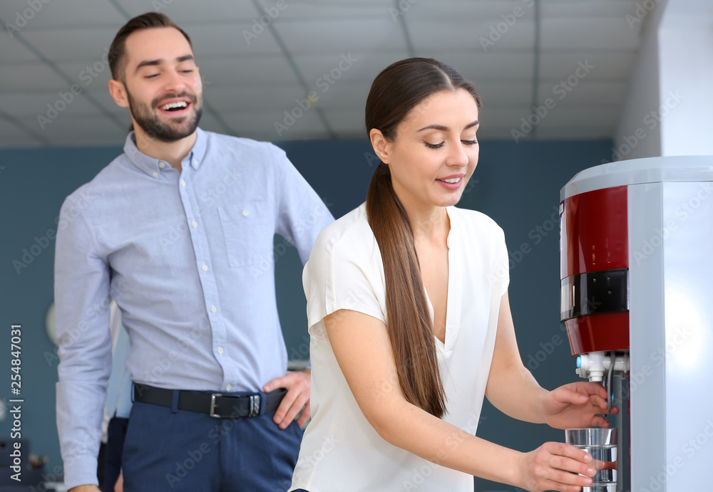 Naklejka premium Colleagues drinking water from cooler in office