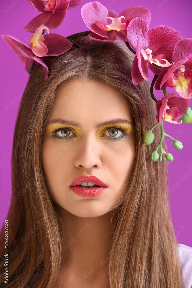 Beautiful young woman with bright makeup and flowers on color background