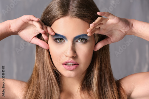 Beautiful young woman with bright makeup on grey background