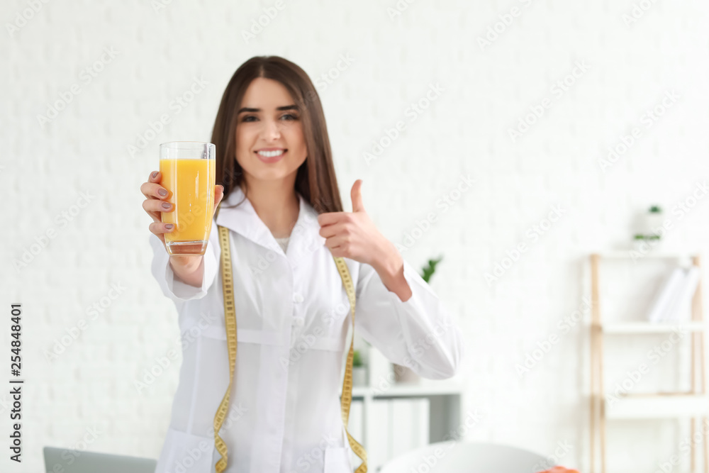 Portrait of female nutritionist with glass of juice showing thumb-up in her office Portrait of female nutritionist with glass of juice showing thumb-up in her office