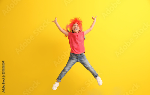 Funny little girl in wig jumping against color background
