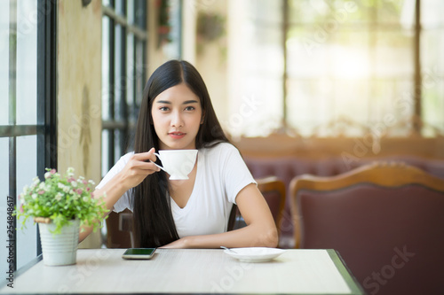 Φωτογραφία A beautiful woman who is sitting drinking coffee near the window with warm sunlight passing through in the morning