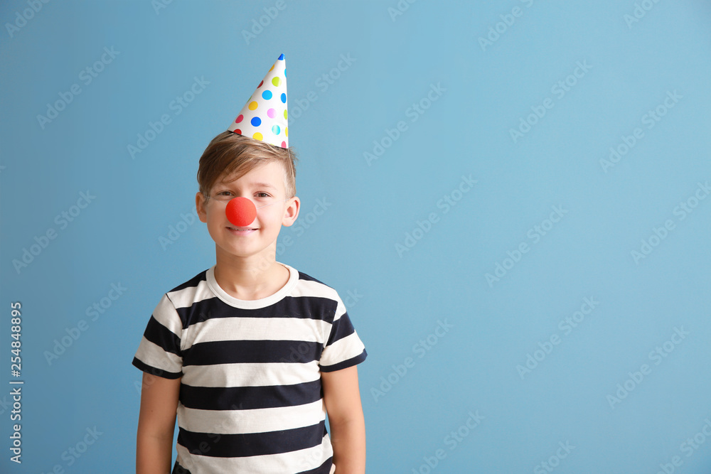 Little boy with clown nose and party hat on color background. April fools' day celebration Little boy with clown nose and party hat on color background. April fools' day celebration