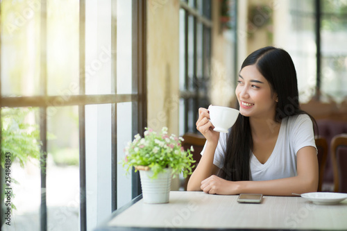 Εκτύπωση καμβά A beautiful woman who is sitting drinking coffee near the window with warm sunlight passing through in the morning