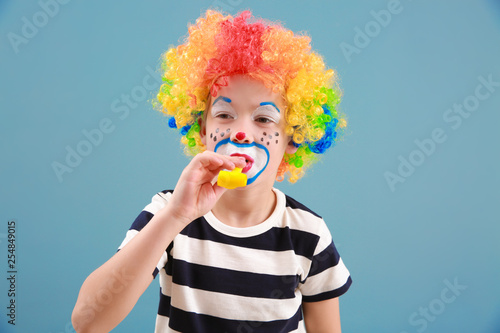 Cute little boy with clown makeup and party whistle on color background. April fools' day celebration