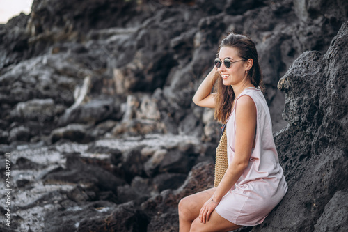 Pretty long hair brunette tourist girl relaxing on the stones near sea.