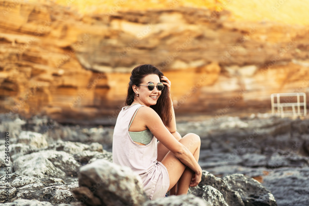 Pretty long hair brunette tourist girl relaxing on the stones near sea. Pretty long hair brunette tourist girl relaxing on the stones near sea.