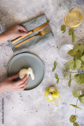 Happy Easter table setting:  mint green plate with  gold cutlery and  woman hands with bunny, painted Egg and wine. Scandinavian style  background with copy space photo