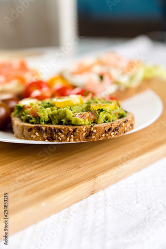 Open sandviches with guacamole, salmon and shrimp and tomato cherry on the plate, wooden background