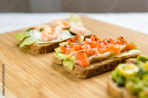 Open sandviches with guacamole, fish and prawn on wood texture  background