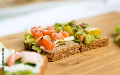 Open sandviches with guacamole, salmon and prawn on wood texture background