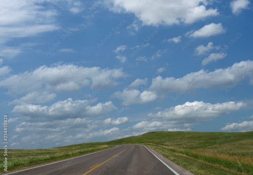 Paved road with green grass and gorgeous skies at the Badlands National Park in South Dakota.