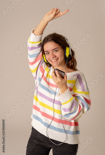 Pretty young teenager girl in headphones listening to music and dancing isolated on grey background © SB Arts Media