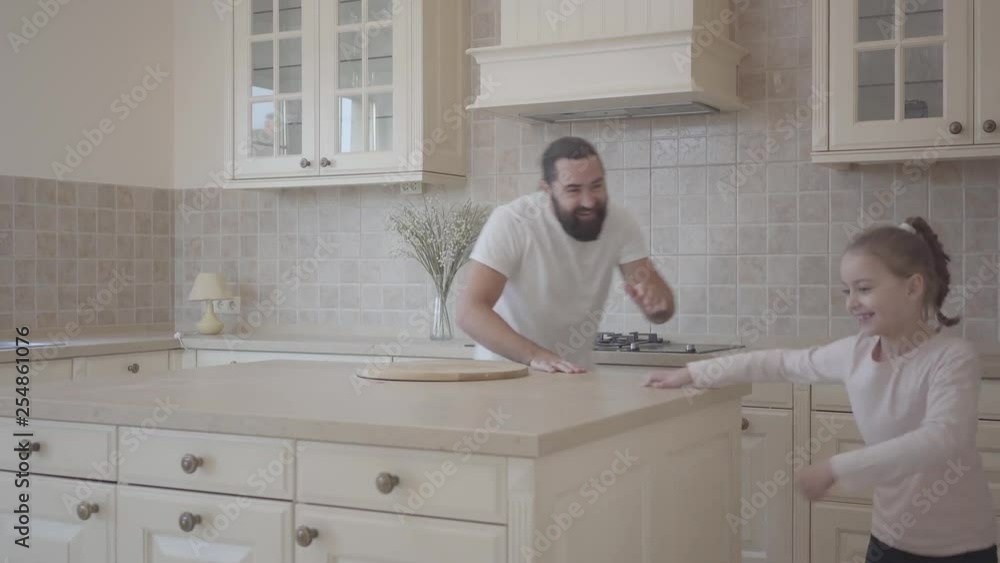 Happy cute daughter and her funny father running, laughing and having fun torether on the beautiful modern kitchen. Father and daughter relationship. A happy family. Happy cute daughter and her funny father running, laughing and having fun torether on the beautiful modern kitchen. Father and daughter relationship. A happy family.