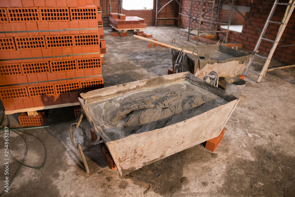 Fototapeta premium Worker shovels a wet mix of concrete from a wheelbarrow at curb block installation. Kerb edging at sidewalk construction.