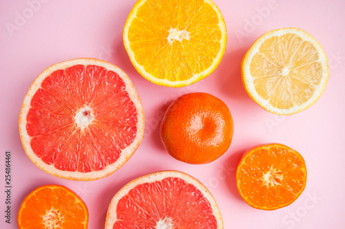 Flat lay of cut ripe juicy citrus fruits on pink background. Citrus pattern.