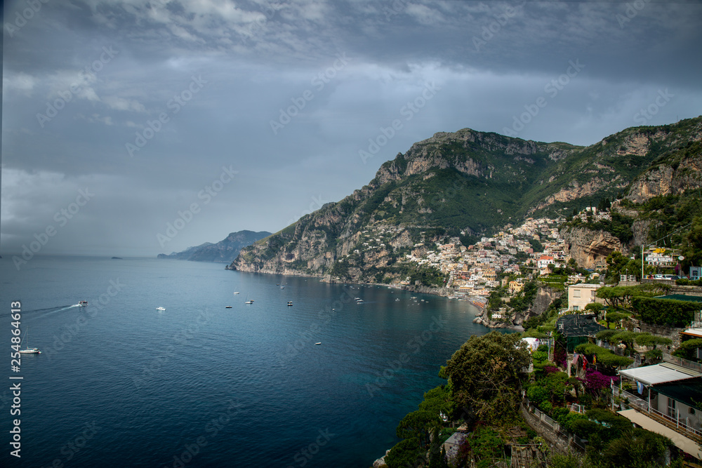 looking back at Amalfi on the Amalfi coast in Italy showing the buildings and house as the rise up the hill with the harbour, blue sea and hills
