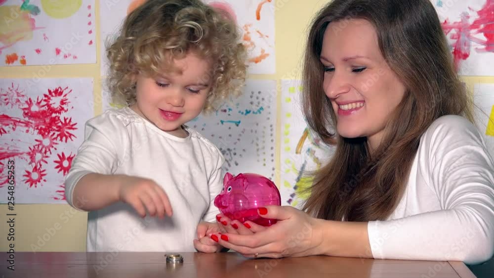 Family girls mother and daughter child having fun putting coins into piggy bank Family girls mother and daughter child having fun putting coins into piggy bank
