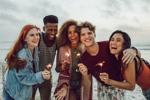 Multiracial friends enjoying at beach with sparklers photo