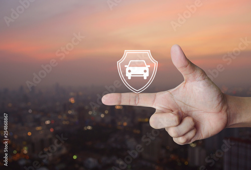 Car with shield flat icon on finger over blur of cityscape on warm light sundown, Business automobile insurance concept