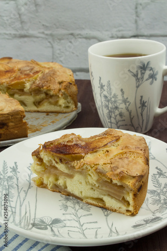 A piece of American apple pie on a white plate with a large white cup of tea