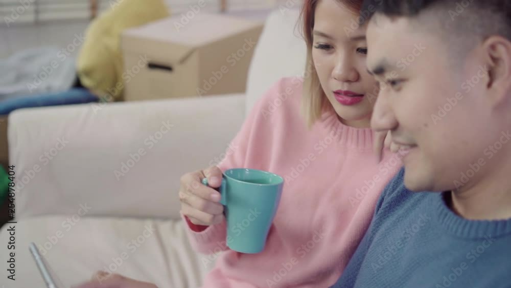 Young Asian couple using tablet and drinking coffee in living room at home, couple enjoy love moment while lying on sofa when relaxed at home. Enjoying time lifestyle family at home concept. Young Asian couple using tablet and drinking coffee in living room at home, couple enjoy love moment while lying on sofa when relaxed at home. Enjoying time lifestyle family at home concept.