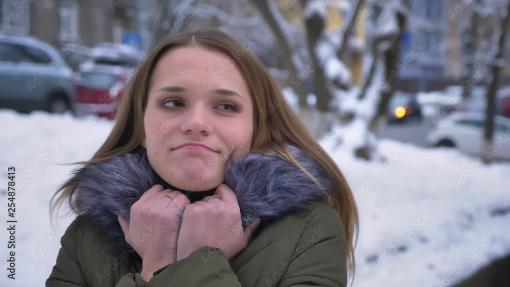 Closeup portrait of young pretty caucasian female with brunette hair being cold and warming her hands in a snowy day Closeup portrait of young pretty caucasian female with brunette hair being cold and warming her hands in a snowy day