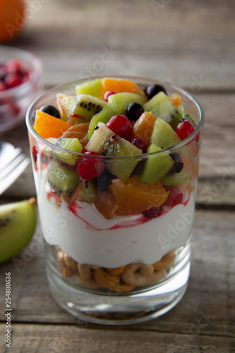 Fresh fruit salad with yogurt and walnuts in glass bowl on stone background. Healthy Eating. Selective focus.