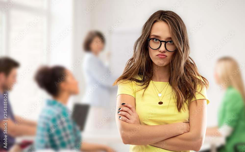 high school, education and human emotions concept - frowning teenage student girl in yellow t-shirt and glasses pouting over classroom and teacher background