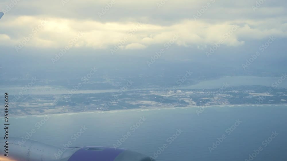 Beautiful view from window flying airplane in cloudy sky over city on sea shore. View from window aircraft flying in sky over sea city. Beautiful view from window flying airplane in cloudy sky over city on sea shore. View from window aircraft flying in sky over sea city.