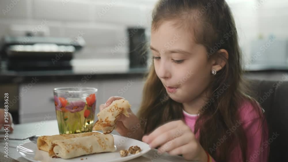 Beautiful little girl eats pancakes and tea at the table. Beautiful little girl eats pancakes and tea at the table.