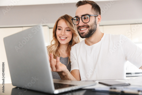 Amazing happy young loving couple sitting at the kitchen using laptop computer.
