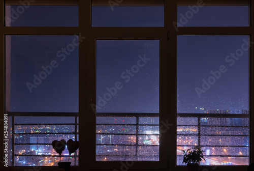 Beautiful night city view from cosy panoramic window with rain drops on it. Kyiv, Ukraine.