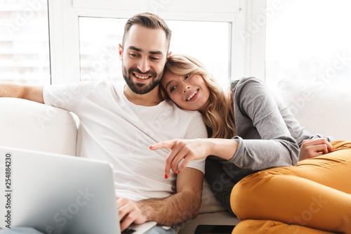 Amazing loving couple sitting indoors at home using laptop computer.