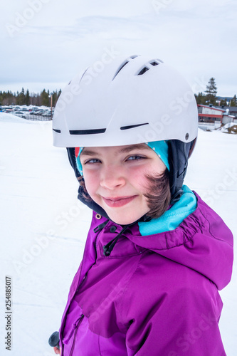 Winter outdoor portrait of a cute young girl in ski outfit and white helmet. © Pebo