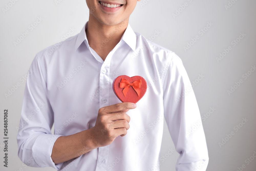 A gift for the beloved. Young beautiful smiling elegant man in a white shirt holding a box with a gift and shows it to the camera. Valentine's Day. A gift for the beloved. Young beautiful smiling elegant man in a white shirt holding a box with a gift and shows it to the camera. Valentine's Day.