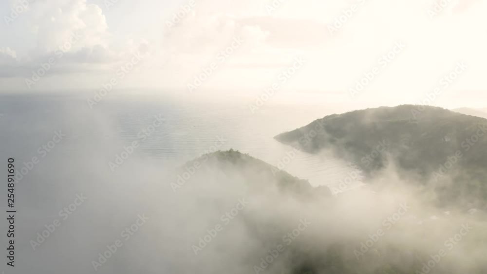 Beautiful drone approaching through the clouds a peak of a tropical forest mountain hiking spot in a summer day with a beach and ocean on the background at sunrise Beautiful drone approaching through the clouds a peak of a tropical forest mountain hiking spot in a summer day with a beach and ocean on the background at sunrise