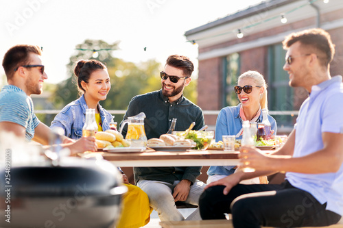 leisure and people concept - happy friends having barbecue party on rooftop in summer