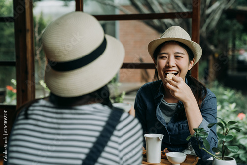 two asian woman travelers in hats sitting in japanese style old wooden house experience culture of sado. happy girl friends chatting laughing while eating sweet snacks drinking matcha green tea teien photo