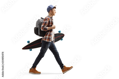 Full length profile shot of a male student walking and holding a longboard isolated on white background
