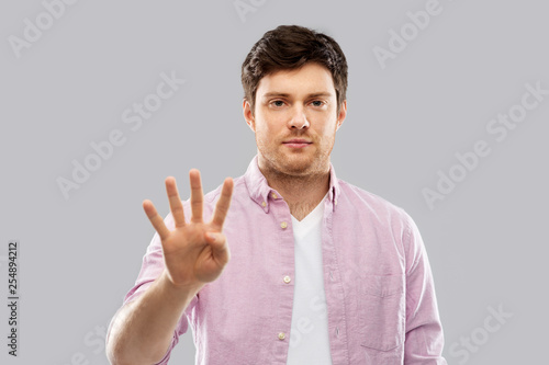 count and people concept - young man showing four fingers over grey background